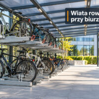 Zadaszona wiata przy biurze z rowerami na dwupoziomowych stojakach i szeroką alejką